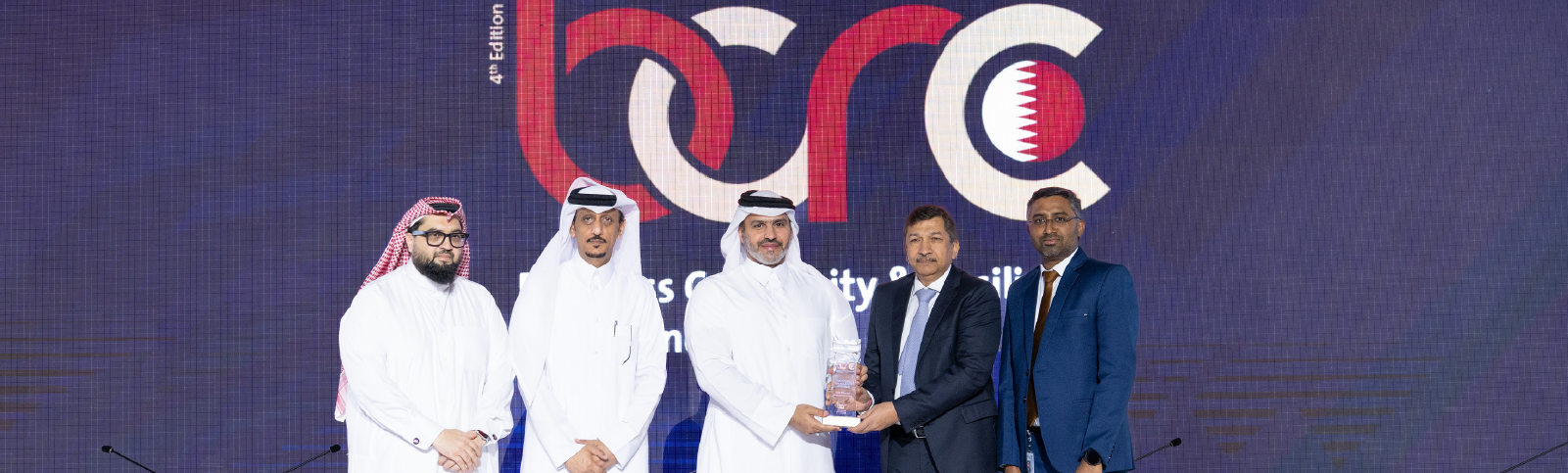 Award handover scene with multiple participants standing in front of an event backdrop.