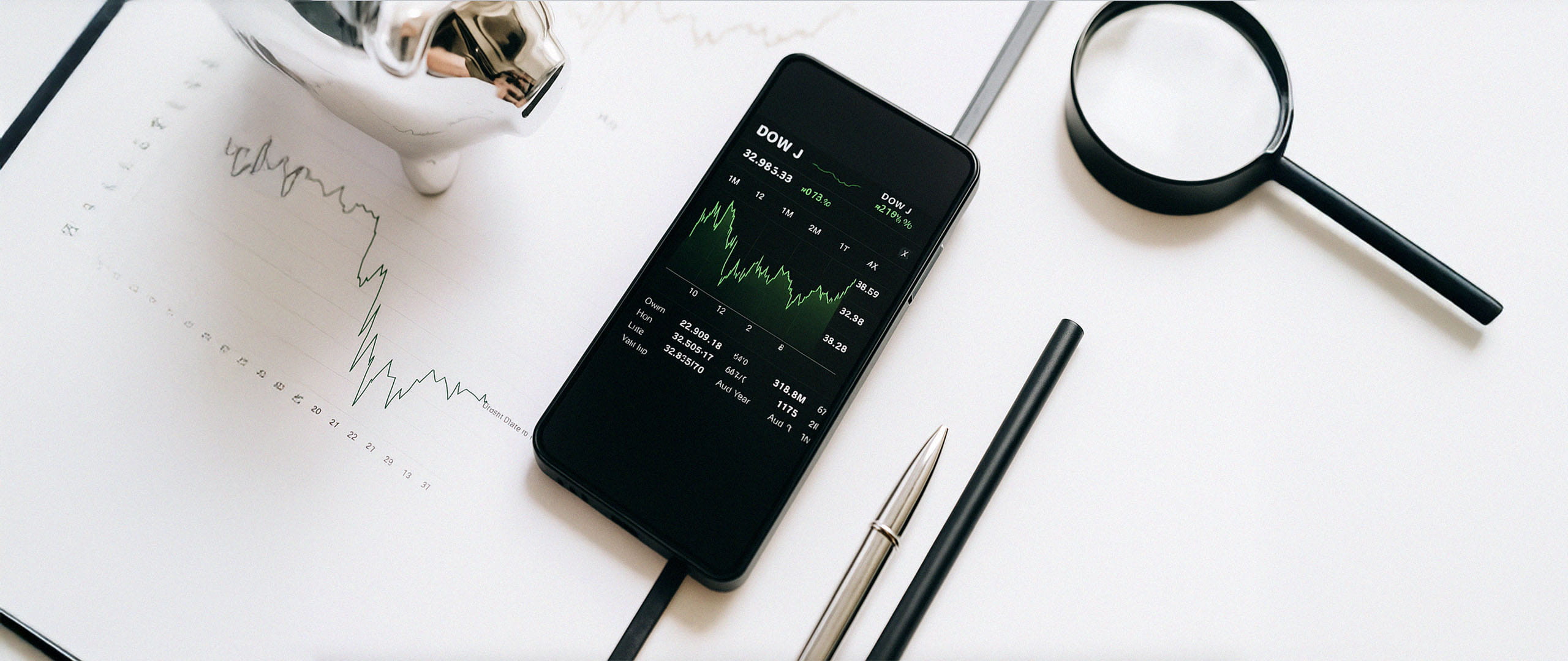 Desk setup with smartphone showing chart, documents, and magnifying glass.